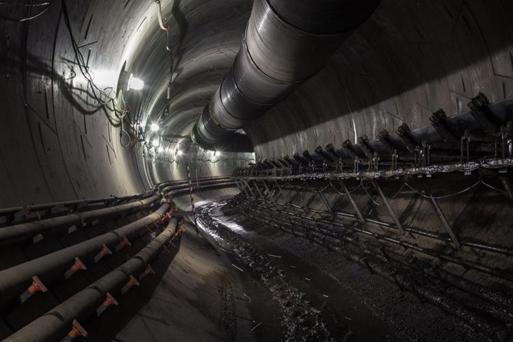 Northbound Central Subway tunnel with curved concrete walls, pipes, and construction equipment visible.