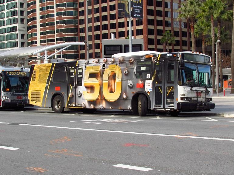Muni bus with Super Bowl 50 gold and black wrap advertisement on city street.