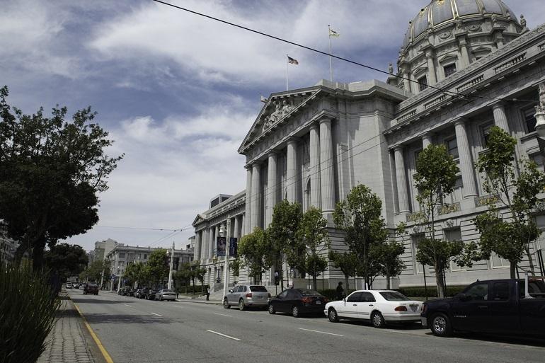 San Francisco City Hall viewed from Van Ness Avenue with parked cars and trees lining the street.