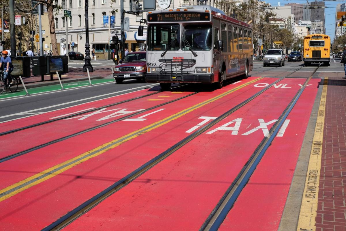 Muni bus traveling in red transit-only lane on Market Street with school bus and pedestrians visible