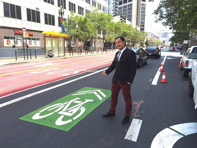 Man in business attire points to green bike sharrow marking on Market Street pavement.