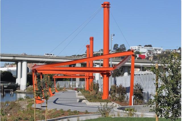 Red steel Liberty Ship art installation at Shoreline Park with bridge and creek visible.