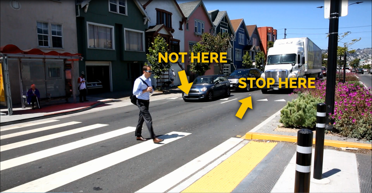 Pedestrian crossing street at marked crosswalk with truck and cars stopped at intersection.