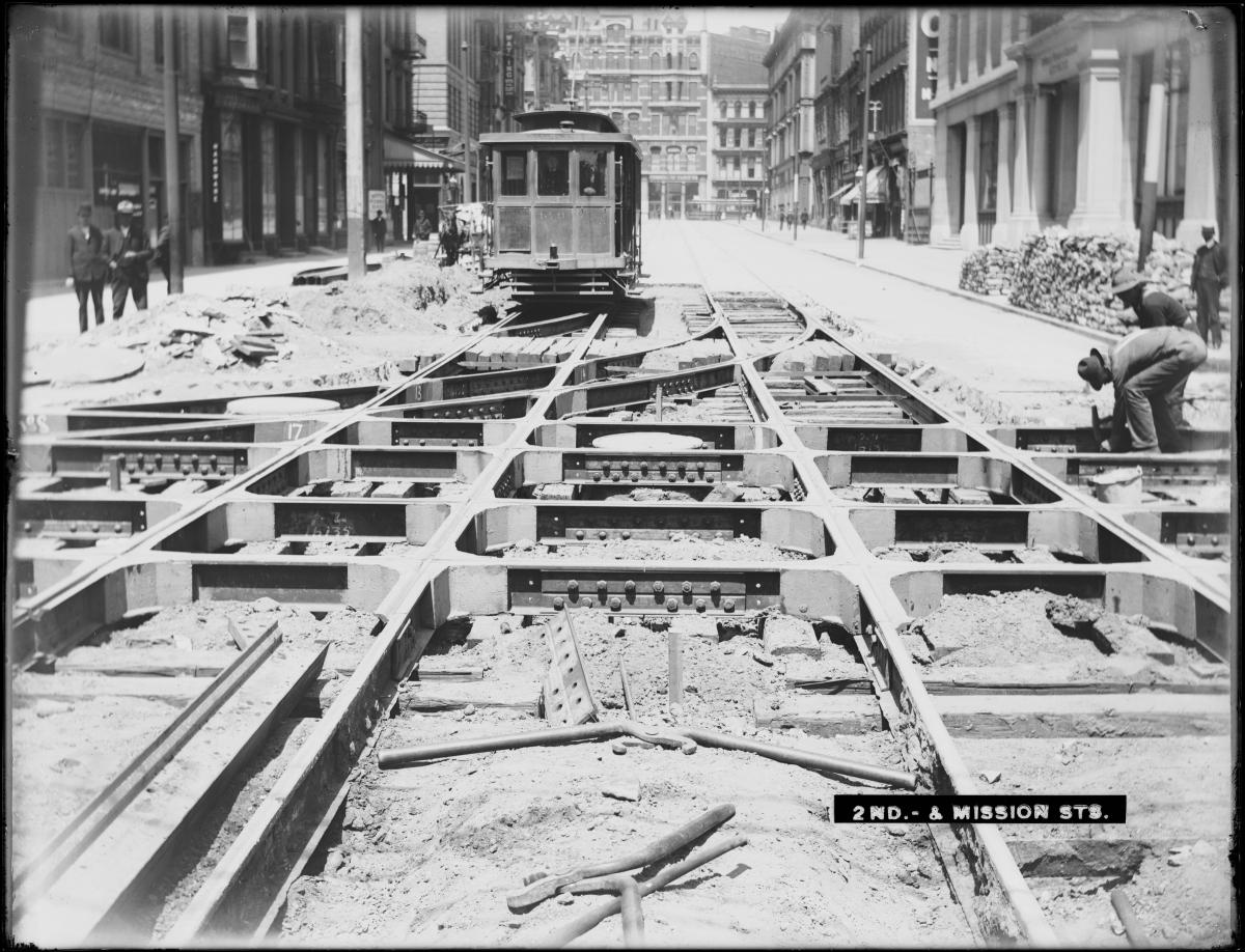 Streetcar 578 approaching track construction at 2nd and Mission Street with workers laying rails in foreground.