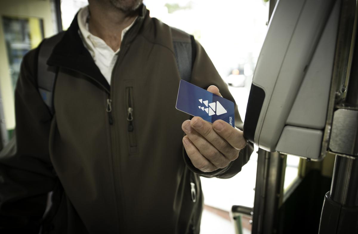 Man in brown jacket holding blue Clipper card near transit reader on streetcar.