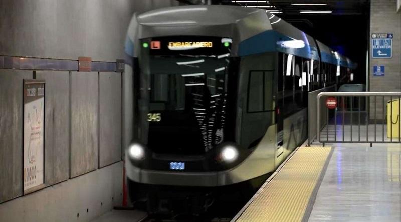 Modern Muni subway train with illuminated headlights entering Civic Center Station platform.