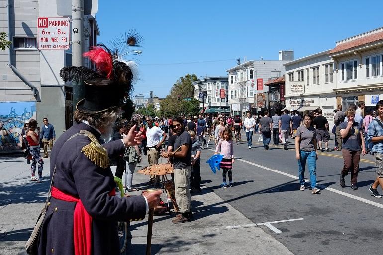 Costumed performer greets pedestrians on closed Valencia Street during Sunday Streets event.