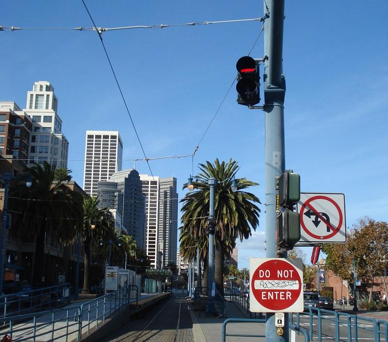 Red traffic signal at intersection with palm trees and downtown buildings in background