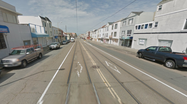 Streetcar tracks running down center of Taraval Street with parked cars and buildings on both sides.
