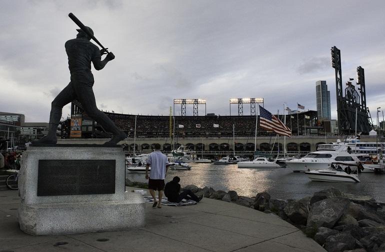 Baseball statue overlooking AT&T Park and McCovey Cove with boats and stadium in background.