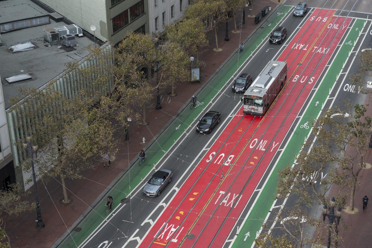 Aerial view of Market Street showing red transit-only lanes, green bike lanes, and a bus traveling downhill with bare trees visible.