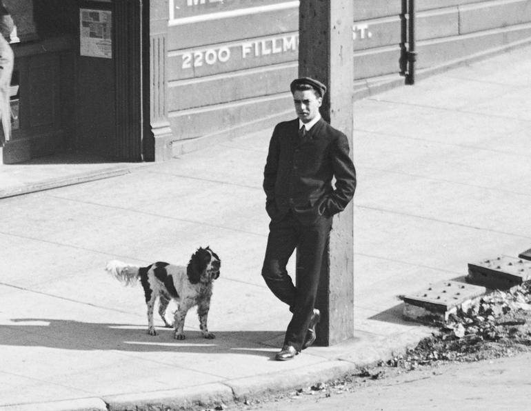 Man in suit standing against pole with spaniel dog on Sacramento and Fillmore Streets, 1905.