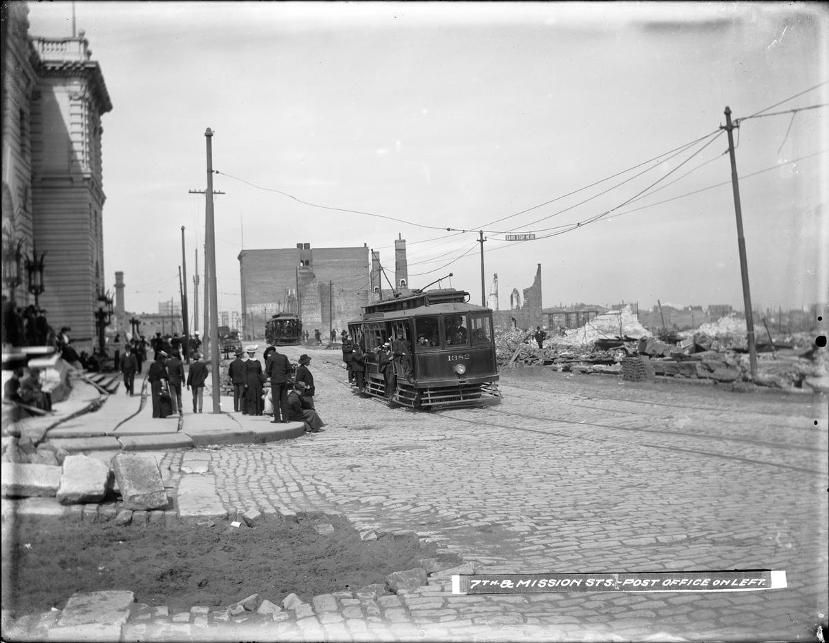 Streetcar 1382 operating on cobblestone street with passengers and damaged buildings in post-earthquake San Francisco, 1906.