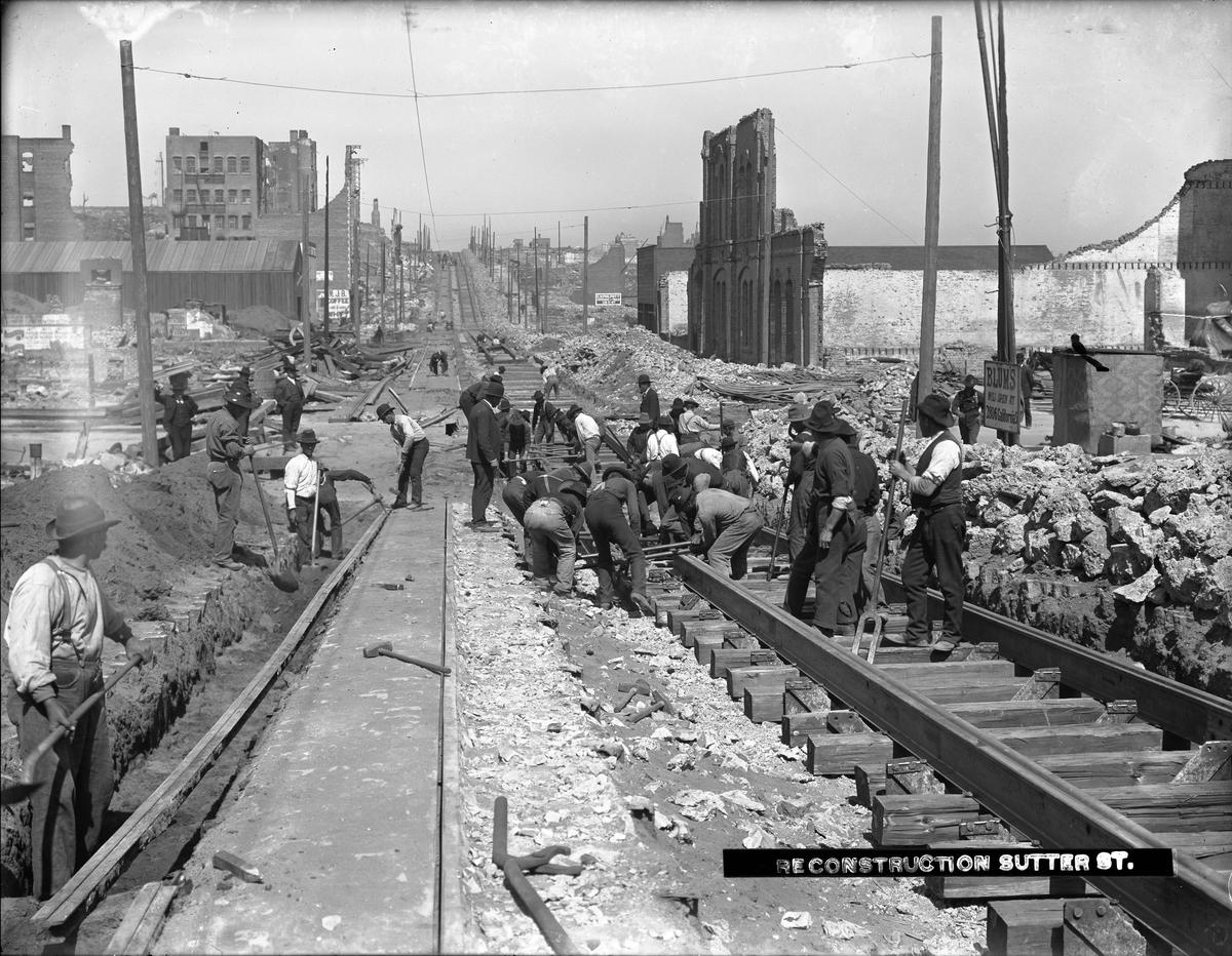 Workers laying streetcar tracks on Sutter Street, San Francisco, June 1906, with city ruins in background.