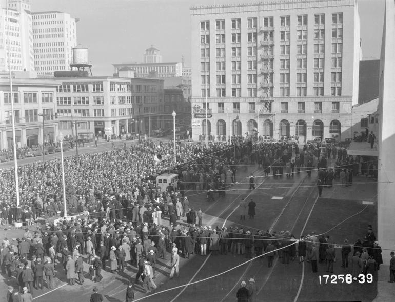Aerial view of large crowd gathered in downtown plaza with Art Deco buildings, 1939.