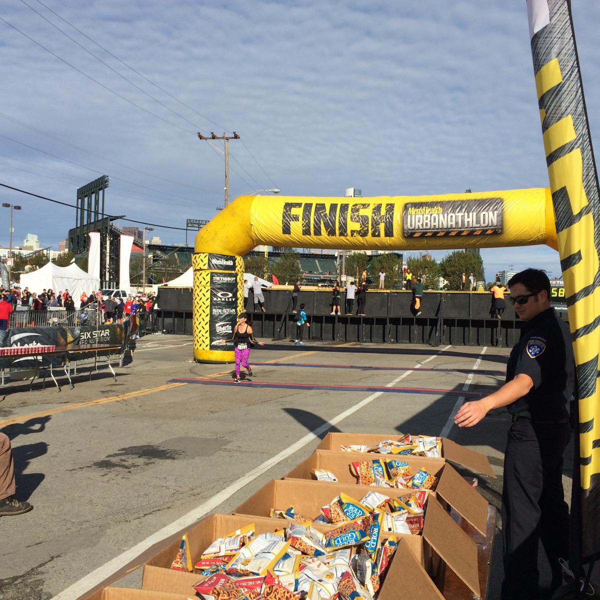 Urbanathlon race finish line with yellow inflatable arch near AT&T Park, competitors and spectators visible.