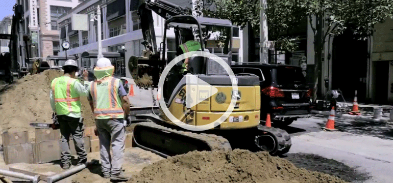 Construction workers and yellow excavator digging in Van Ness Avenue median near O'Farrell Street.