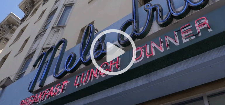 Mel's Diner neon sign on Van Ness Avenue with blue and red lettering on storefront.