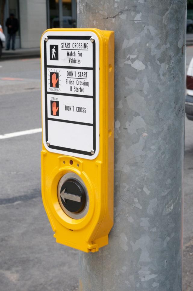 Yellow accessible pedestrian signal mounted on pole with tactile button and audible crossing instructions.