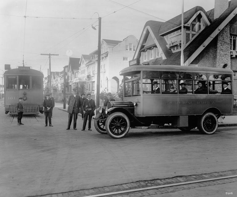 Vintage bus and streetcar with uniformed operators and passengers at urban street corner, 1917.