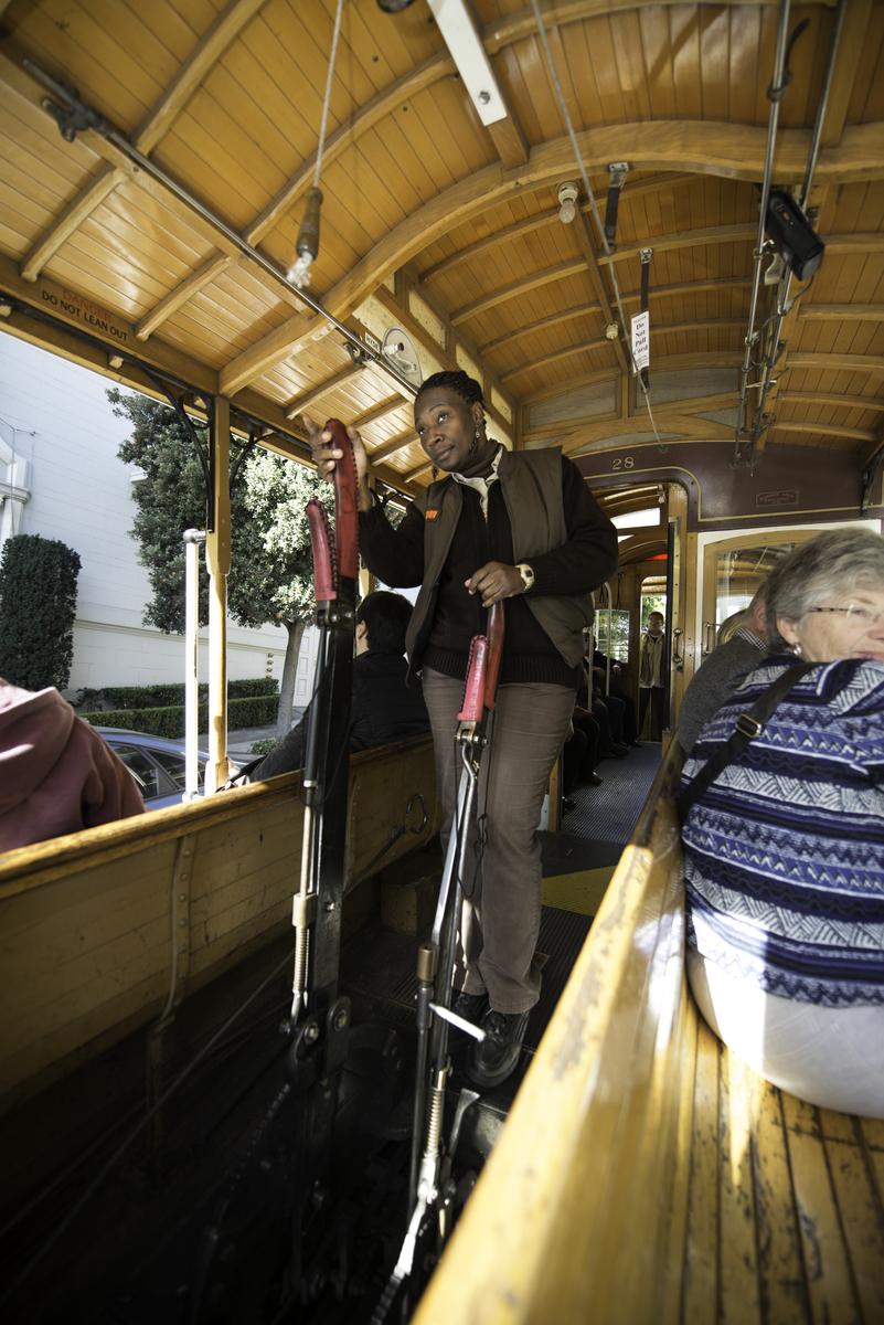 Cable car operator gripping the brake lever inside a wooden cable car with passengers.