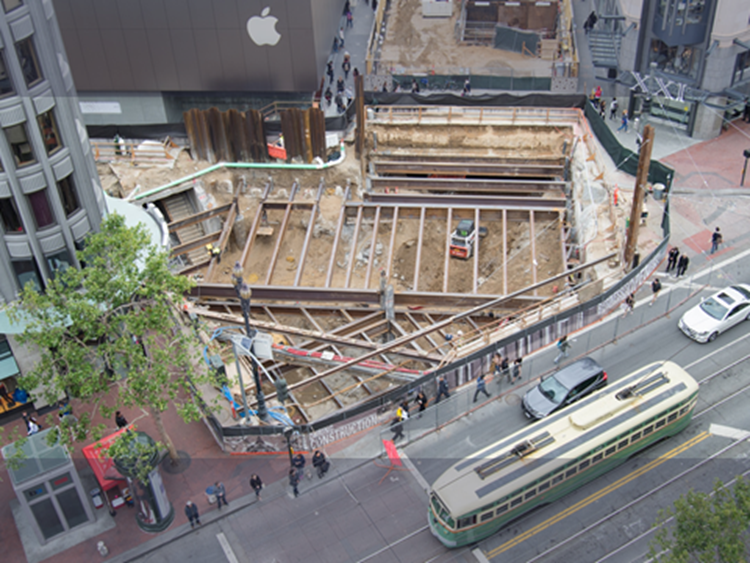 Aerial view of underground construction site at Market and Stockton streets with streetcar and pedestrians nearby.