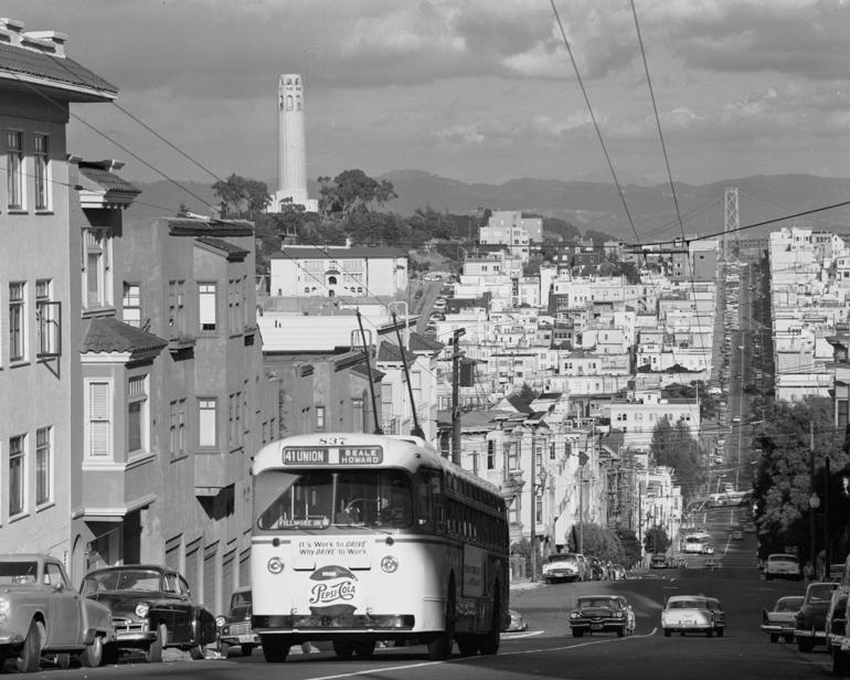 Trolley bus climbing Russian Hill on Union Street with North Beach neighborhood and Coit Tower in background, 1957.