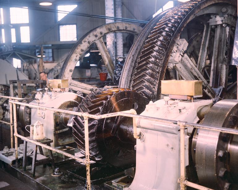 Large industrial gears and pulleys of worn cable winding machinery in factory setting.