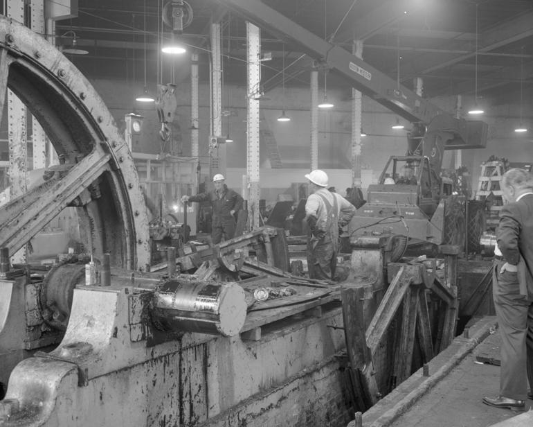 Workers disassemble cable drive sheaves in industrial workshop, 1965.