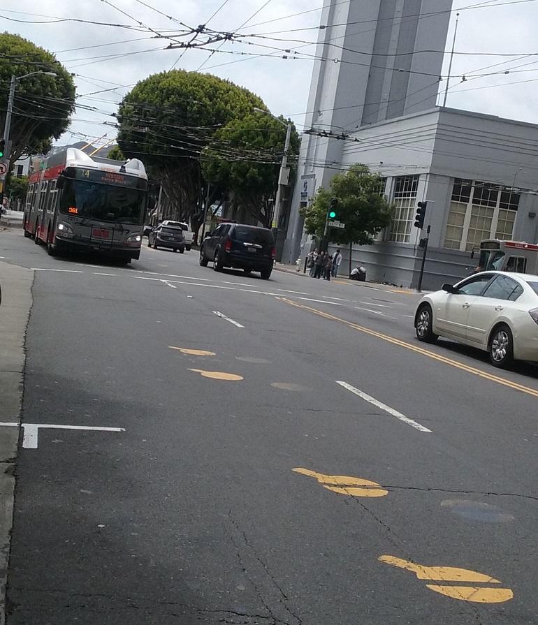 Electric trolley bus approaching yellow dot pavement markings at Mission and 11th streets intersection.