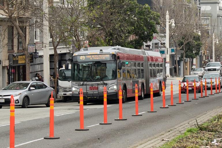 Route 49 bus traveling northbound on Van Ness Avenue with traffic control cones lining the street.