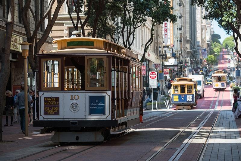 Cable car number 10 traveling down Powell Street with trees and downtown buildings in background.