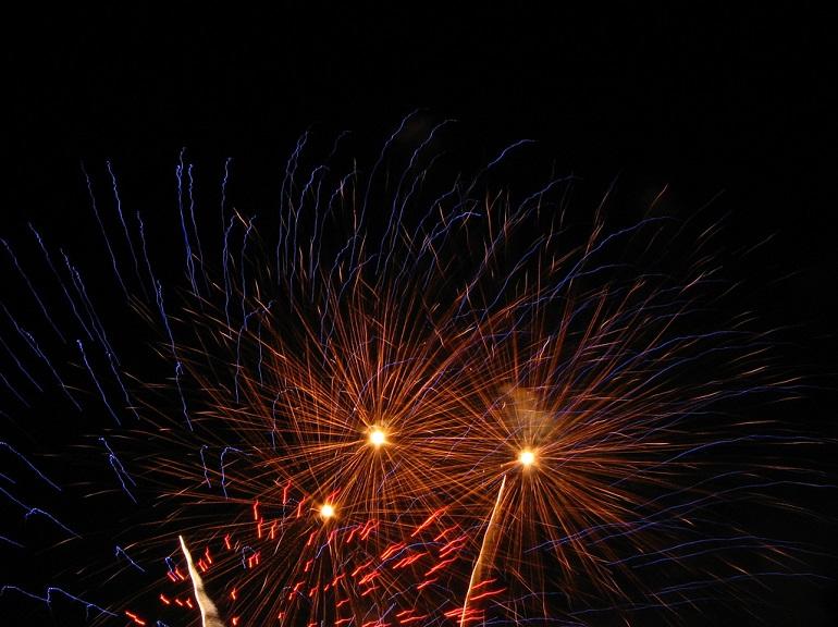 Colorful fireworks bursting against a dark night sky with red, orange, and blue sparks radiating outward.