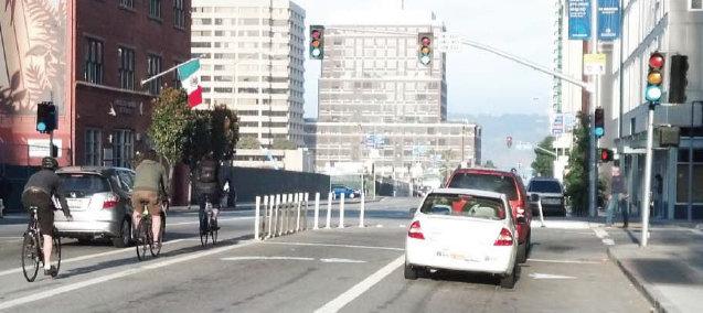 Cyclists and cars on Folsom Street with white protective barriers separating bike lane from traffic.
