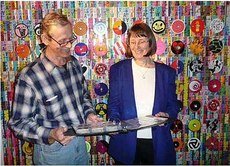 Two people examine a collection of colorful transit passes displayed on a wall behind them.