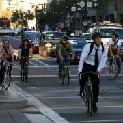 Multiple cyclists riding on Market Street during commute hours with pedestrians and vehicles visible.