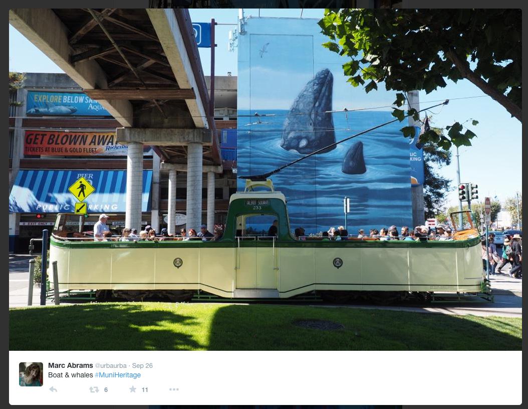 Green vintage streetcar with whale mural backdrop under highway overpass