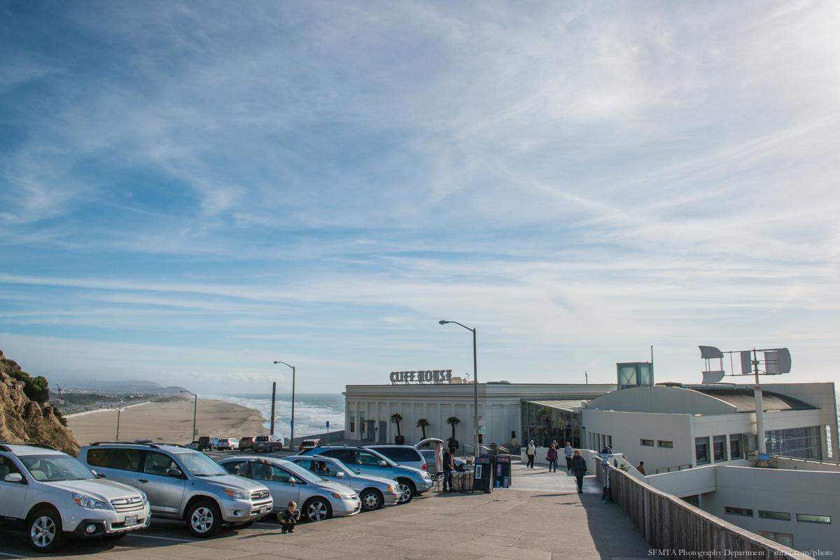 Cliff House building with parked cars and visitors on a sunny day overlooking Ocean Beach