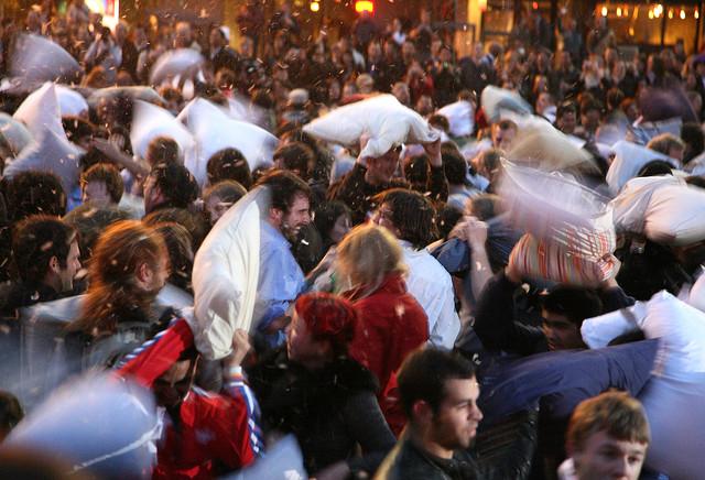 Large crowd of people engaged in a pillow fight with feathers flying through the air at night.