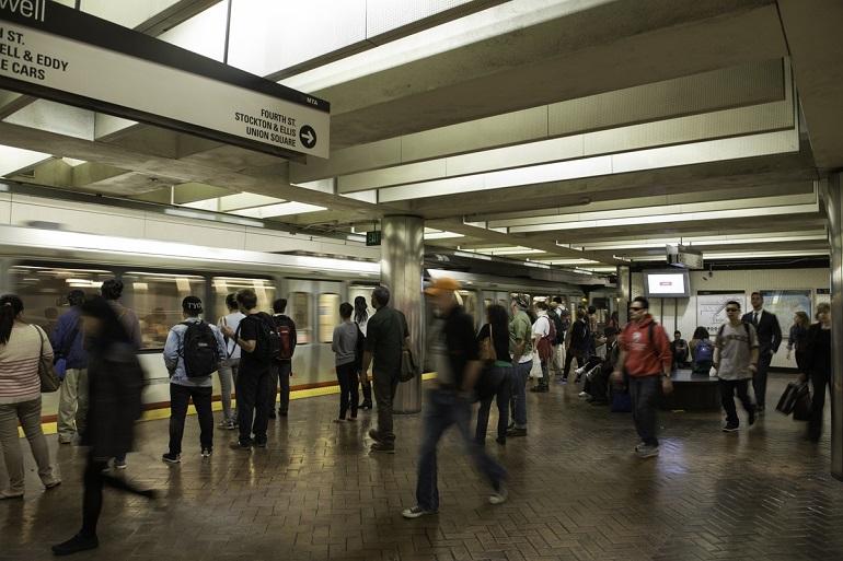 Commuters wait on platform at Powell Muni Metro Station with train stopped at station.