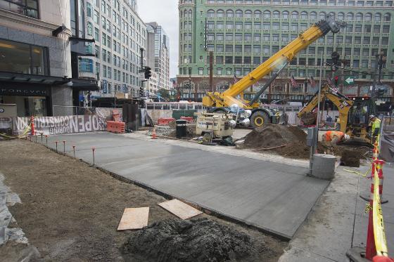 Construction site at Stockton Street with poured cement walkway, crane, and surrounding urban buildings.
