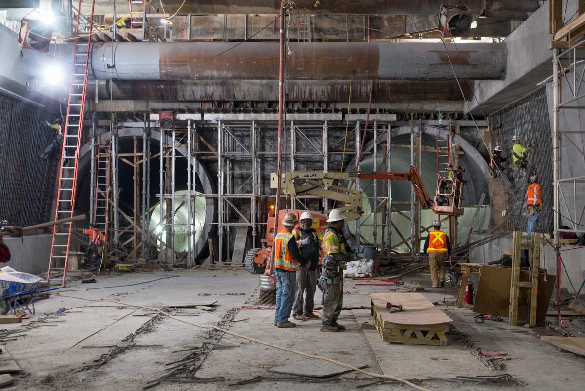 Construction workers in safety gear work on underground transit tunnel renovation with scaffolding and equipment visible.