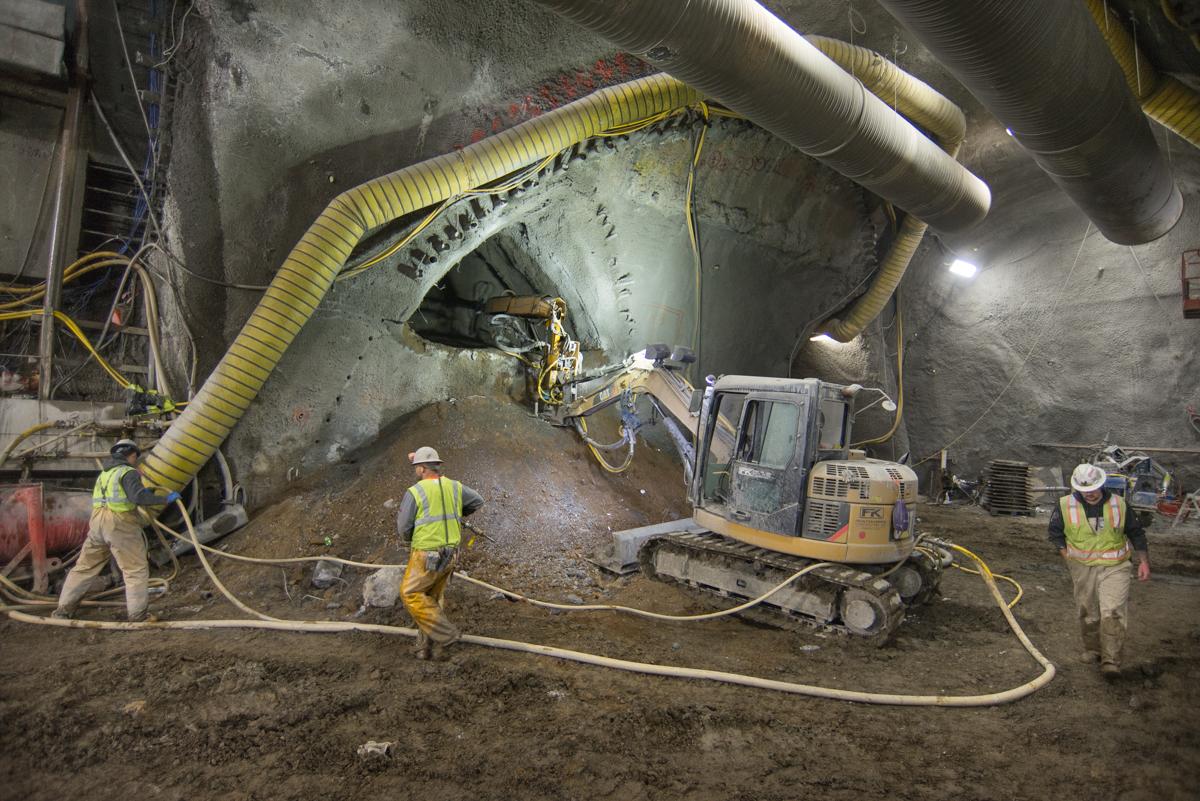 Workers operate excavation equipment inside underground tunnel cavern during transit construction project.