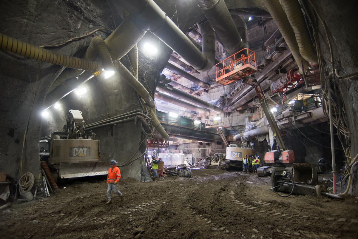 Underground construction site with workers, CAT equipment, and lit tunnel cavern during platform excavation.
