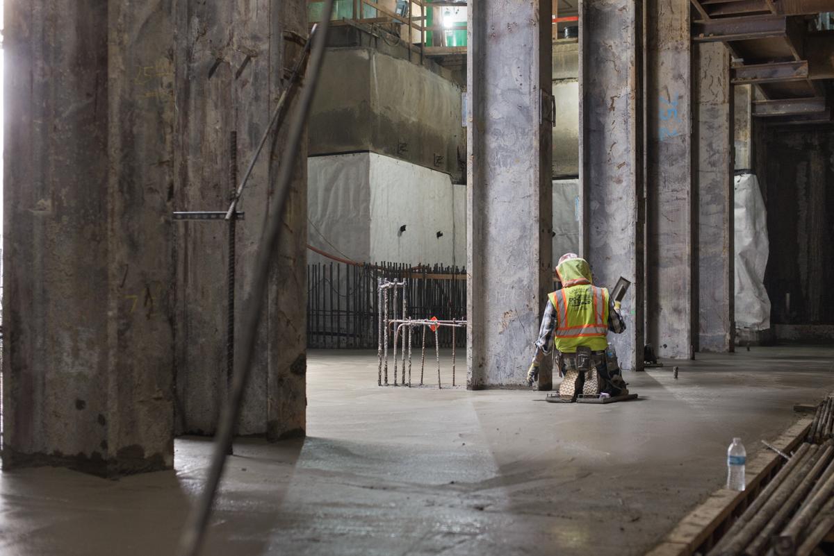Worker in safety vest smoothing freshly poured concrete in underground transit station under construction.