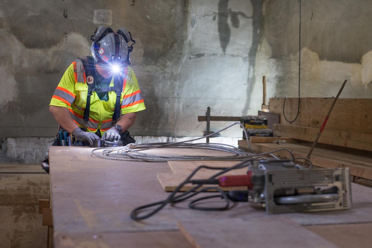 Worker in safety vest and headlamp assembling concrete forms and electrical conduit in underground station construction area.
