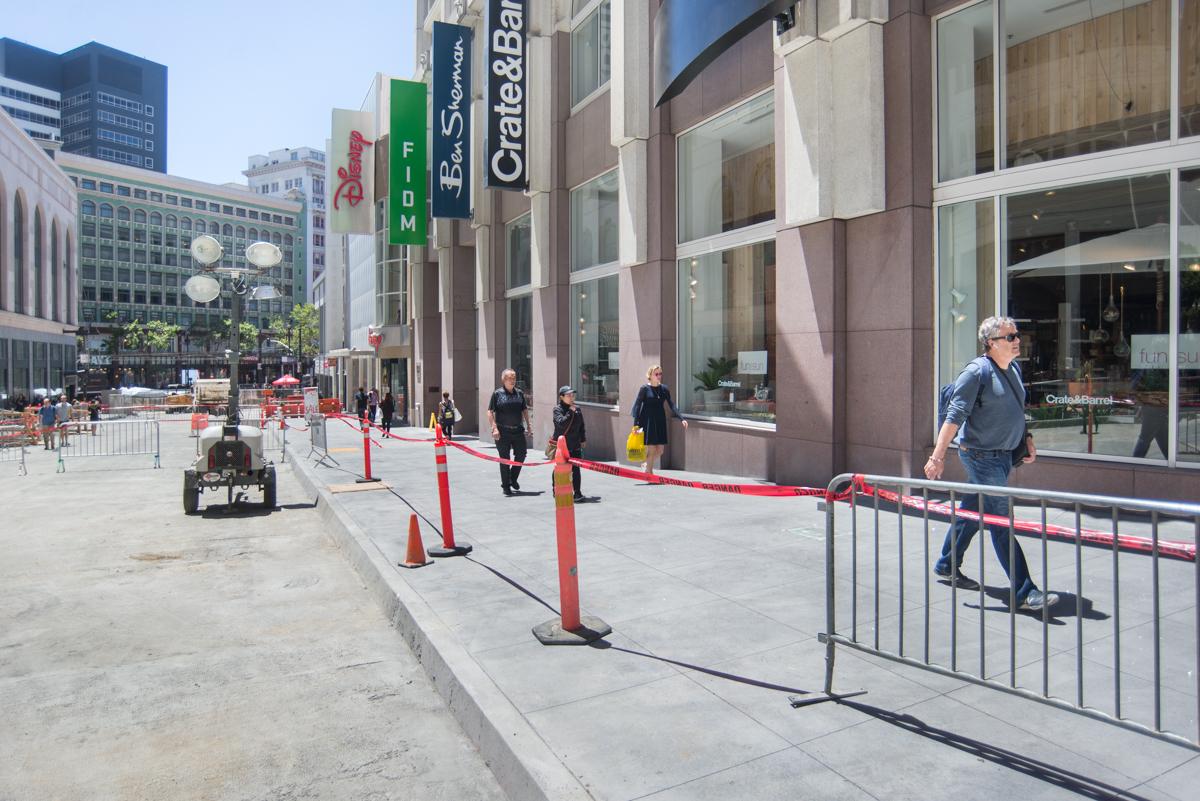 Reconstructed west sidewalk on Stockton Street with barriers, pedestrians, and storefronts visible.