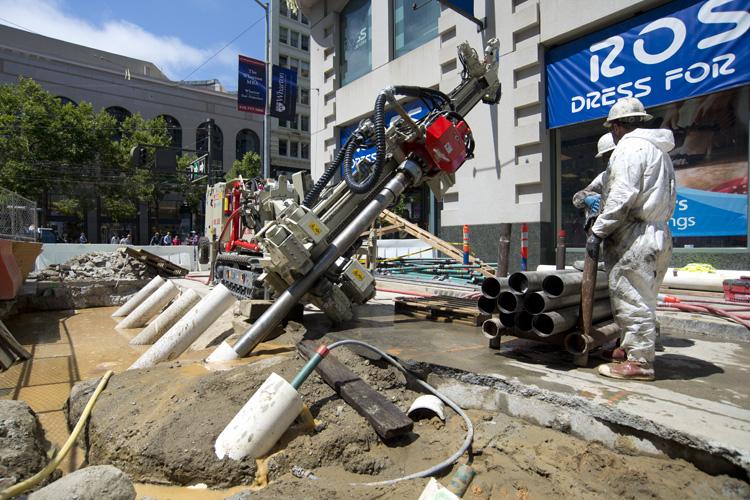 Construction worker in protective suit operating compensation grouting equipment at 4th and Market Street intersection.
