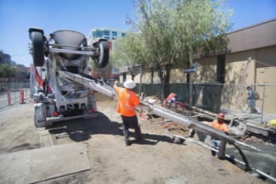 Worker in orange vest operating concrete mixer truck at utility construction site on city street.
