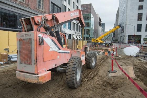 Red telehandler lifting equipment at urban construction site on 4th Street.